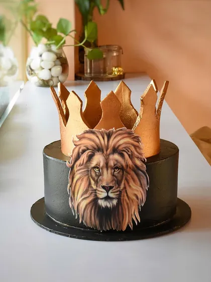 A feast for a king. This bold cake features a metallic black finish, an edible image of a lion's face, and is topped with a striking golden crown, perfect for someone with a commanding presence.