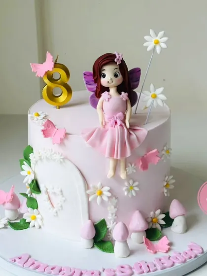 An enchanting fairy-themed cake for an 8th birthday, featuring a handcrafted fondant fairy, delicate butterflies, and whimsical mushrooms. The soft pink and white colors create a magical woodland scene.