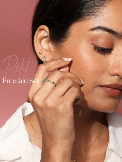 A model wearing the Petit Emerald Set, which includes a ring and huggie earrings. This set features Zambian emeralds set in gold, crafted for a timeless glow.