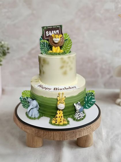 A stylish two-tier jungle safari cake. The modern design features an ombre green effect and cute fondant animals like a lion, giraffe, elephant, and zebra.