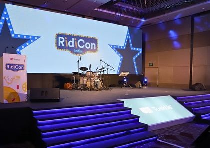 Another view of the 'RidiCon' stage, showing the illuminated steps and branded lectern. The entire setup is designed to be immersive and reinforce the event's brand identity.