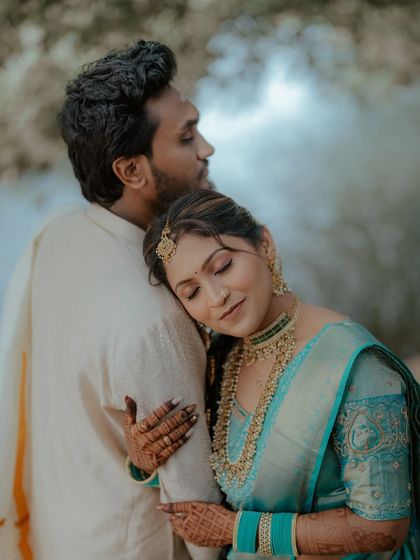 A romantic couple shot capturing a tender moment. The bride's South Indian look, with her elaborate jewelry and hairstyle, is showcased beautifully.