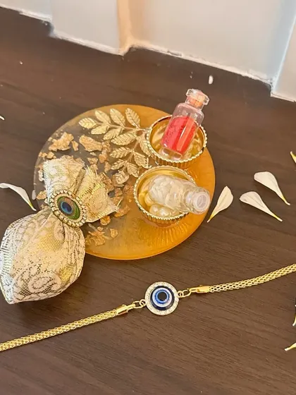 This modern evil eye rakhi is paired with a matching resin thaali and a small potli for shagun. It's a chic and complete set for a contemporary Rakhi celebration.