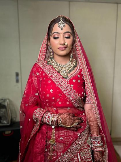 A front view of the bride, showing how the elegant twisted bun and floral arrangement complete her stunning red bridal lehenga look.