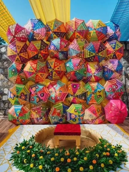For a truly unique and colorful backdrop, we can create a wall made entirely of traditional Rajasthani embroidered umbrellas. This design is perfect for a vibrant Mehendi party and serves as a fantastic photo opportunity.