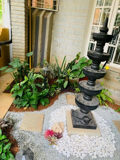 Another angle of the Deepa Stambha garden, showing the layout of the plants and hardscaping. The design creates a natural flow and highlights the traditional lamp post as the centerpiece.