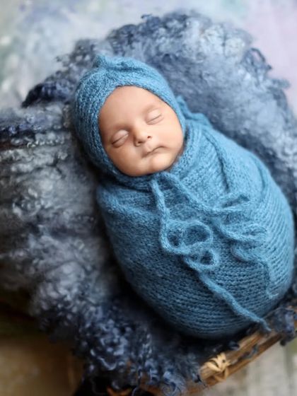 A cozy and simple portrait. The baby is swaddled in a blue knit wrap and matching bonnet, nestled in a basket with soft, textured layers.