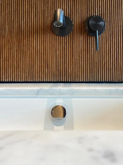 In this bathroom detail, the cool, clean lines of the marble sink and countertop are contrasted with the warmth of a fluted wood backsplash. The modern black fixtures from Gessi provide a sharp, graphic accent.