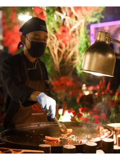 A chef tends to sizzling items on a large tawa grill. The dramatic lighting and rich colours of the surrounding decor highlight the premium atmosphere of our events.