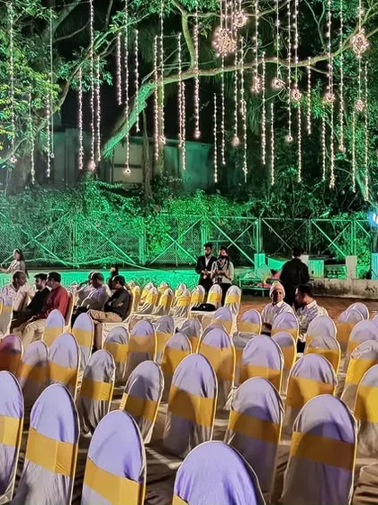 A wide shot of an outdoor event space, showing the stage and guest seating under a canopy of hanging lights.