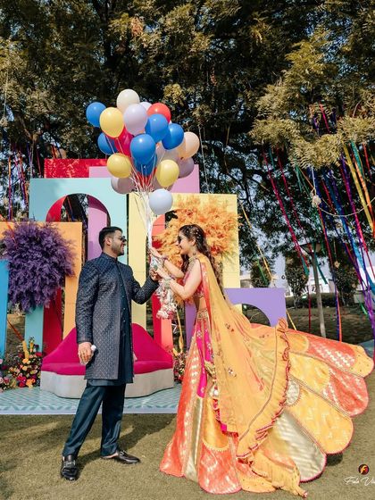 A beautiful, dynamic shot of the couple with balloons and a flowing dupatta against a colorful backdrop, capturing the festive spirit of their Mehendi.