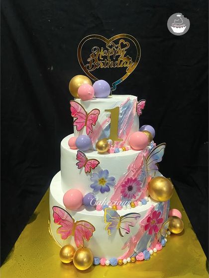 A grand three-tier cake for a very special first birthday. Adorned with butterflies and pastel spheres, this cake is designed to be a showstopper.