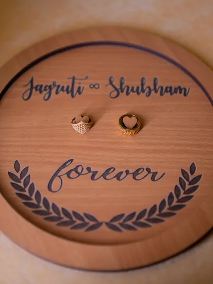 A detail shot of the couple's engagement rings on a custom-engraved wooden platter. I always make sure to capture the personalized details that make your day unique.