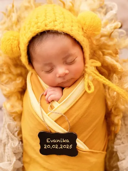 A close-up of a sleeping newborn with a small plaque marking her birth date. These personalized details make your baby's first photos even more special.