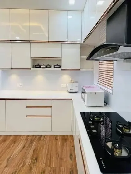 A look at a finished modular kitchen, combining style and function. This design features high-gloss white cabinets, a sleek black chimney, and a durable countertop, all built for modern living and daily use.