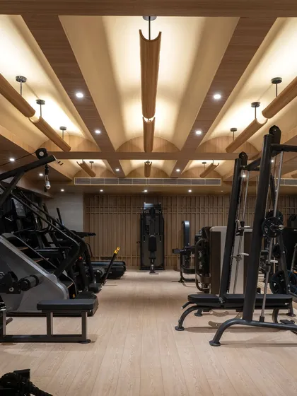 At the BeWell wellness studio, the gymnasium is sculpted from wood and light. The coffered ceiling with its custom light fixtures creates a warm, rhythmic canopy over the state-of-the-art equipment, transforming a functional space into a serene architectural experience.
