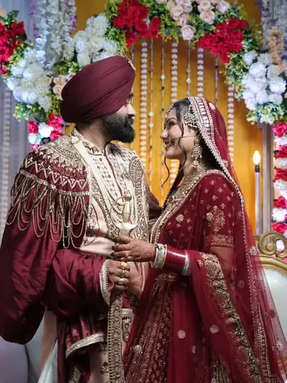 A regal portrait of a Sikh couple on their wedding stage, dressed in rich maroon and gold attire.