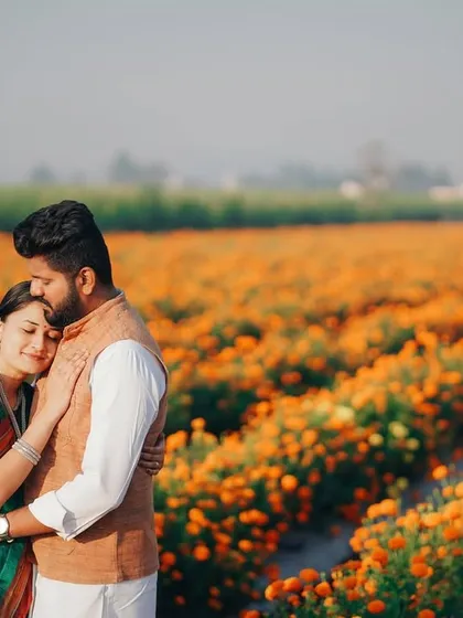 A tender moment of embrace during a pre-wedding shoot. The soft morning light and the warm colors of the marigold field create a beautifully romantic and serene atmosphere for this candid portrait.