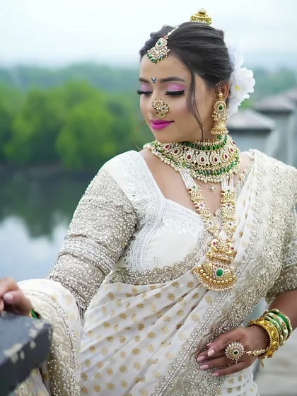 A serene portrait of a bride in a white traditional saree. The outdoor setting by the water adds a beautiful, natural element to this classic Maharashtrian look.