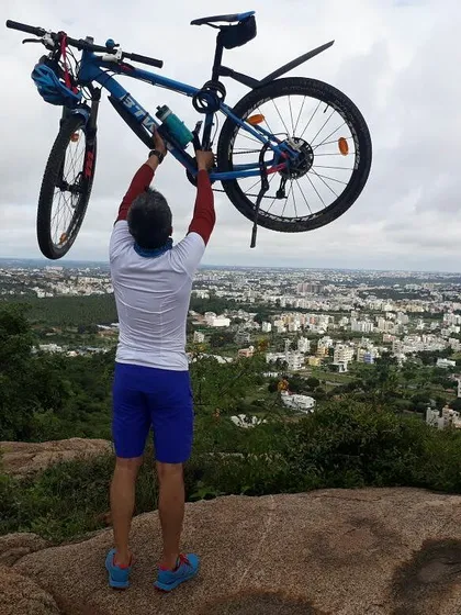 A rider holding his bike aloft, overlooking the vast Bangalore cityscape from a hilltop.