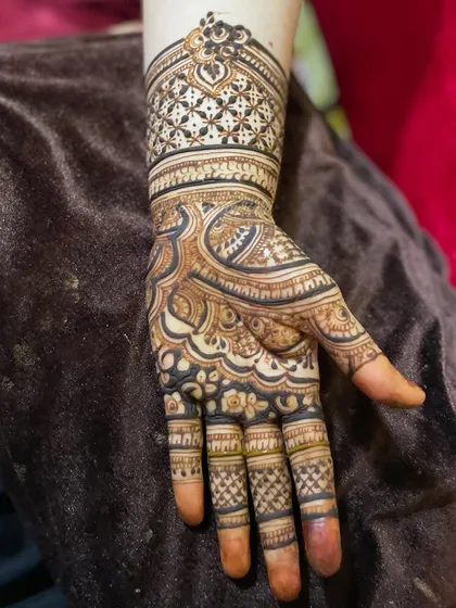 A close-up of a single hand, showing the combination of bold, dark patterns and delicate, fine-line details. The wristband features a heavy checkerboard pattern for a strong visual anchor.