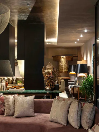 A reflection of the living room, showing the layered arrangement of furniture, lighting, and art. A large Garuda sculpture adds a touch of mythological grandeur to the eclectic space.