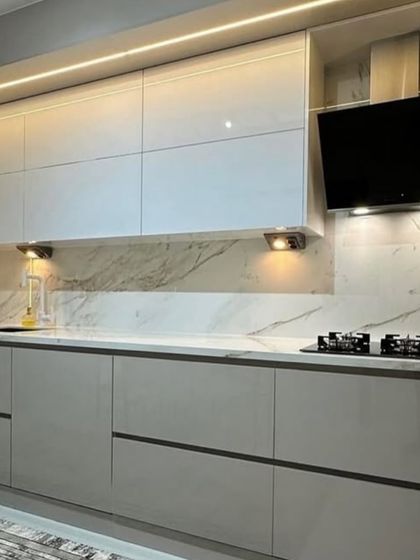 A sleek kitchen design featuring a wall-mounted television, perfect for catching up on news or shows while cooking. The handle-less cabinets and marble-patterned backsplash add to the modern, clean aesthetic.
