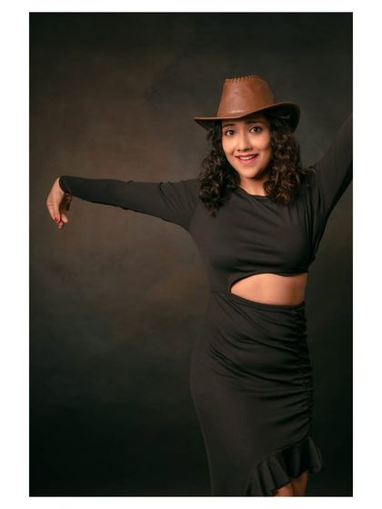 A playful and energetic portrait of a model in a black dress and cowboy hat. Her pose captures a moment of dance and celebration.
