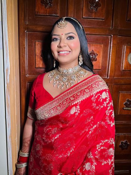A beautiful client, Kavya, ready for a wedding event in a stunning red saree. Her makeup is classic and radiant.