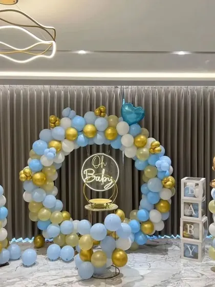This "Oh Baby" themed baby shower is a classic and elegant choice. The setup features a full balloon ring in a soft blue, white, and gold palette, complemented by a neon sign, "BABY" blocks, and themed balloon pillars.