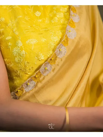 A detailed view of the delicate self-thread floral embroidery on a lime yellow blouse. The neckline is adorned with handcrafted floral tassels, adding a touch of whimsical elegance.