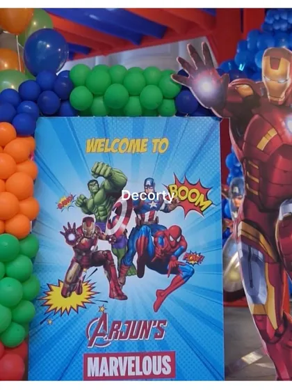 A "Welcome to Arjun's Marvelous" party sign, framed by colorful balloons and a life-sized Iron Man cutout.