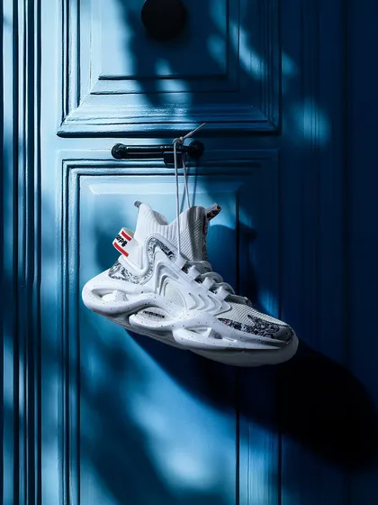 A single white sneaker hanging on a blue door. The strong contrast, shadows, and simple composition create a striking and artistic image that is highly memorable.