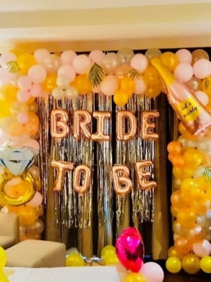 A vibrant and fun "Bride to be" backdrop. This design uses a silver tinsel curtain framed by a colorful balloon arch in yellow and pink, with large foil balloons spelling out the occasion.