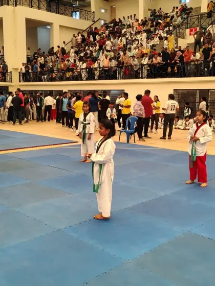 A student stands ready on the competition mat, focused and prepared to demonstrate her Poomsae (forms) in front of a large crowd.
