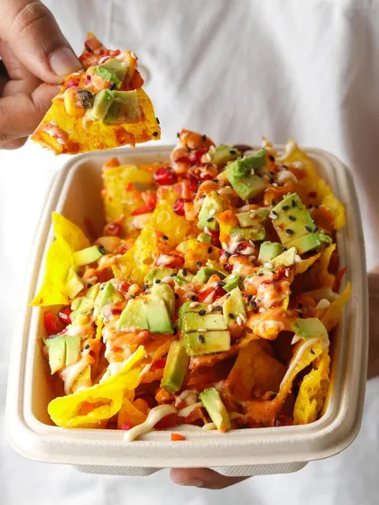 A hand holding up a single, loaded wonton nacho, showcasing all the fresh toppings like avocado and salmon.