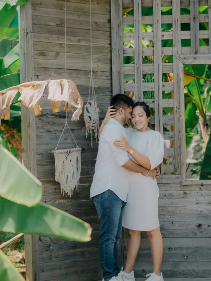 A tender embrace against a rustic wooden wall with bohemian-style decor. This setting provides a trendy and warm backdrop for a pre-wedding shoot.