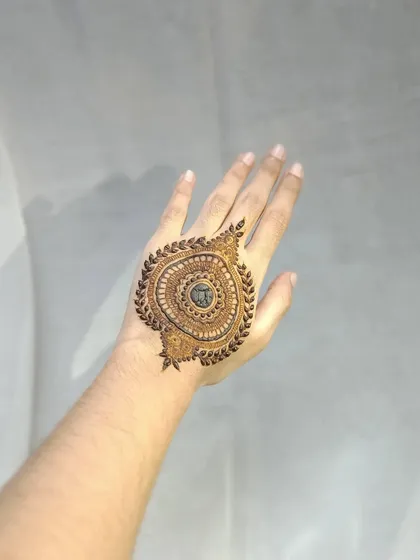 A bold mandala design on the back of the hand, framed with a border of leaves. The center is left open for the dark stain to create a powerful contrast.