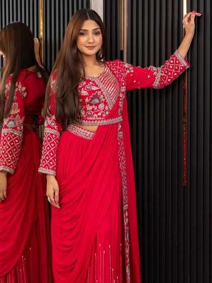The full look of our red draped saree set. The jacket-style blouse and pre-draped skirt create a powerful and fashionable statement, perfect for a wedding guest.