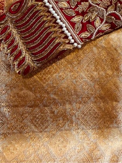 A close-up of the rich texture created by hand embroidery on a red bridal blouse. The raised threadwork and bead detailing add depth and luxury to the design.