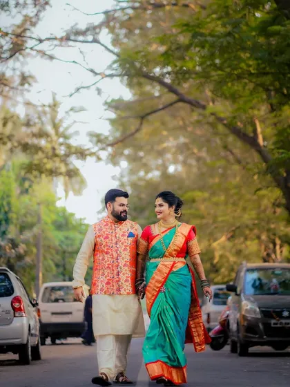 A full-length shot of a couple in vibrant Maharashtrian traditional attire, walking down a tree-lined street. This blends tradition with a modern, urban setting.