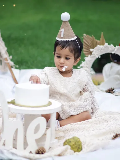 A gentle and sweet cake smash moment. This little one is delicately touching her first birthday cake in our outdoor boho-themed setup.