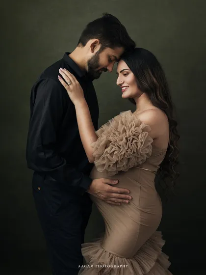 An elegant fine art maternity portrait of a couple, showcasing a classic, painterly style against a dark, textured backdrop. The focus is on their connection and the beautiful anticipation of new life.