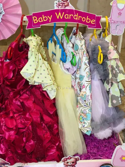 The 'Baby Wardrobe' cart for a twin girls' gift set, showcasing a beautiful collection of party dresses and casual wear on tiny hangers.