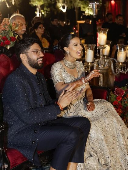 A candid moment of the couple enjoying the Sangeet performances. The bride's makeup looks flawless even from a distance.