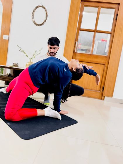 Assisting in a variation of Camel Pose, supporting the student's back to encourage a deeper, more open heart-opening posture.