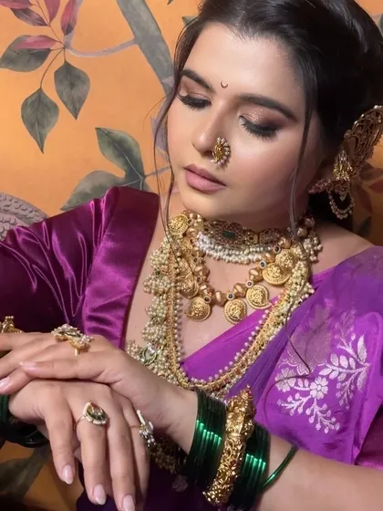 The rich temple jewelry against the purple nauvari saree creates a stunning contrast. The makeup features smoky eyes and a defined lip, adding to the regal feel of the ensemble.