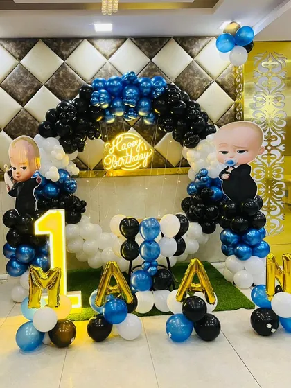 This is a duplicate of ID 30, 208, 220, 248, 253. A classic Boss Baby theme for a first birthday. This setup includes a balloon arch in blue, black, and white, character cutouts, a 'Happy Birthday' neon sign, and a light-up number '1'.
