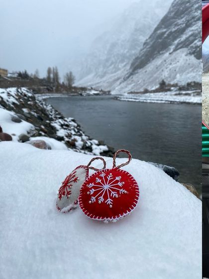 Red and white Christmas ornaments resting on fresh snow by a river in the mountains.