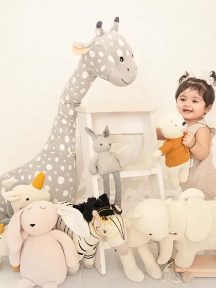 A toddler girl surrounded by an array of stuffed safari animals, perfect for a "wild one" or animal-themed shoot.